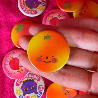 Badge orange/ Prix (sans les frais de ports): 5€/ Taille: 38mm de diamètre/ Matériaux: Aluminium